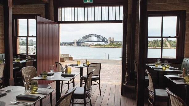 An outdoor dining area with tables and chairs, overlooking a bridge and water. - Beautiful Balmain East Cottage (Balmain East)