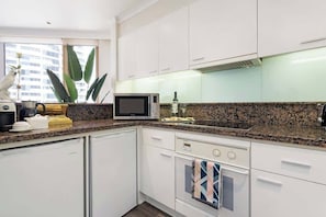 Una cocina moderna con armarios blancos, microondas, cafetera y escurreplatos.