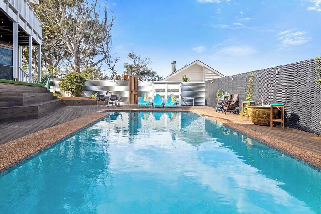 A swimming pool with a wooden deck, a white fence, and a house in the background.
