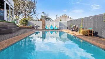 A swimming pool with a wooden deck, a white fence, and a house in the background.