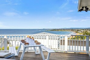 Eine Holzterrasse mit weißer Reling mit Blick auf Strand und Meer.