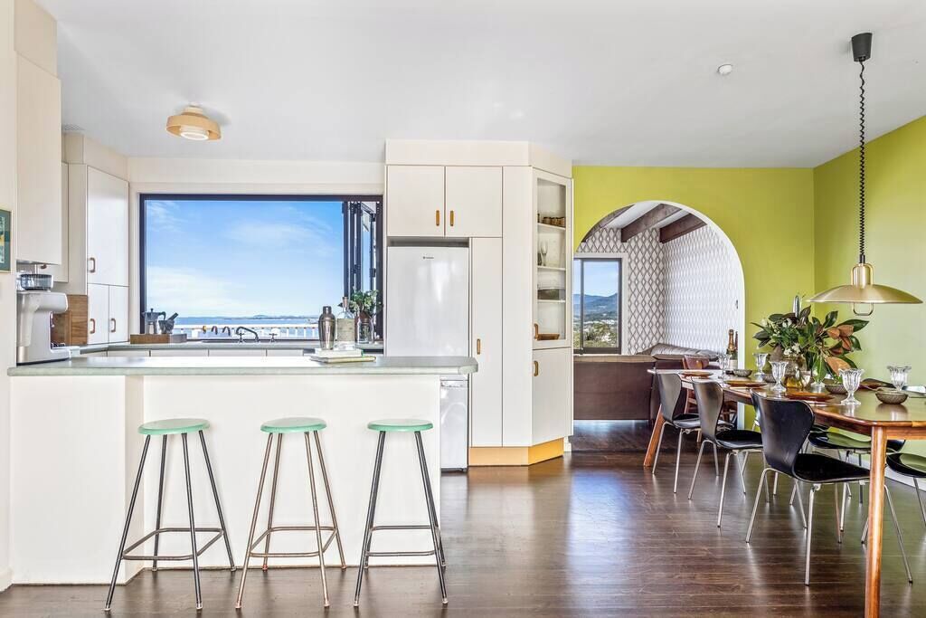 A modern kitchen with a large window, white cabinets, and a dining area with a table and chairs.
