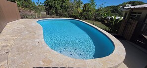 A rectangular swimming pool with clear blue water, surrounded by a stone deck and a metal fence.