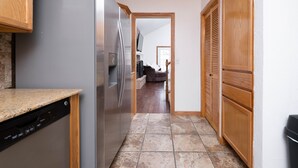 Una cocina con lavavajillas integrado, refrigerador de acero inoxidable, gabinetes de madera y piso de baldosas.
