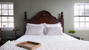 Una cama bien hecha con sábanas blancas y una bandeja de madera sobre una alfombra mullida y blanca.