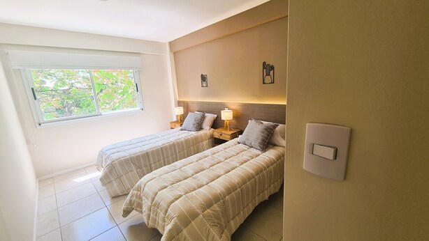 Una camera da letto con due letti, una finestra con vista sul verde e un interruttore della luce fissato al muro.