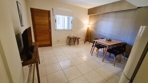 Una cucina compatta con una porta in legno, un piccolo tavolo da pranzo con sedie, un frigorifero e una finestra con persiane.