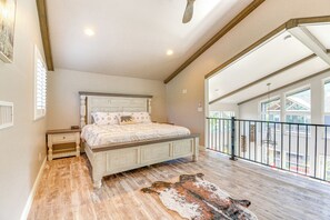 A bedroom with a large bed, a nightstand, a wooden floor, and a view of the outside through a balcony. - Hot Tub + Deck: Mtn-View Pine Getaway! (Pine)
