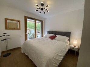 Un dormitorio con una cama grande, una lámpara de techo, una mesita de noche y una ventana con vistas a la vegetación.