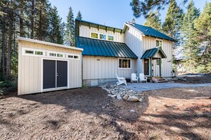 Une maison à deux étages avec un toit en métal, un garage et un patio doté d’un espace salon extérieur.
