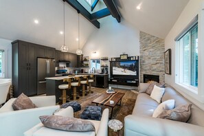 Uma sala de estar moderna com lareira, cozinha com armários escuros e uma grande tela de TV.