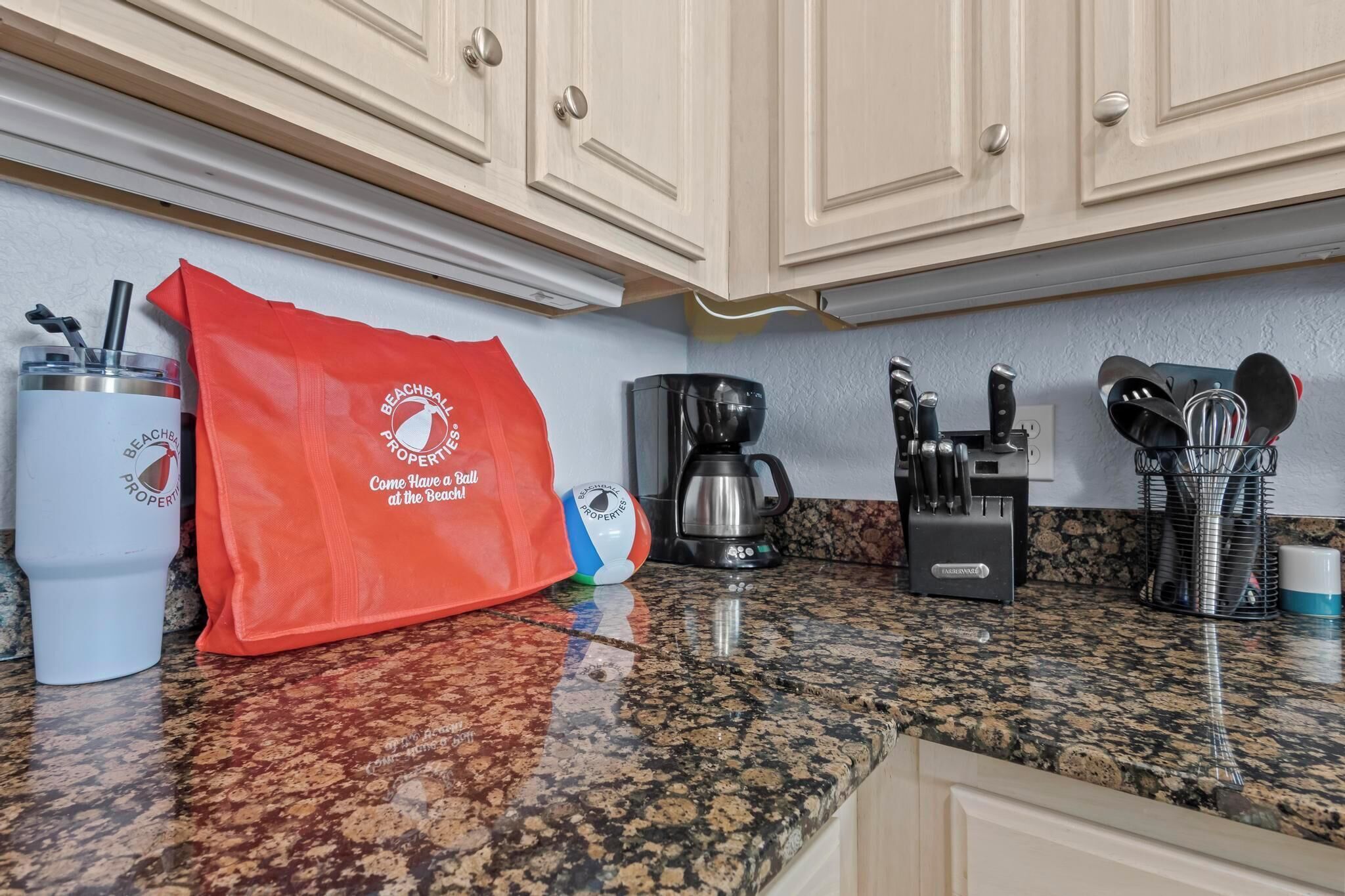 A kitchen with granite countertops, a coffee maker, a knife block, and a bag with a beach-themed logo.