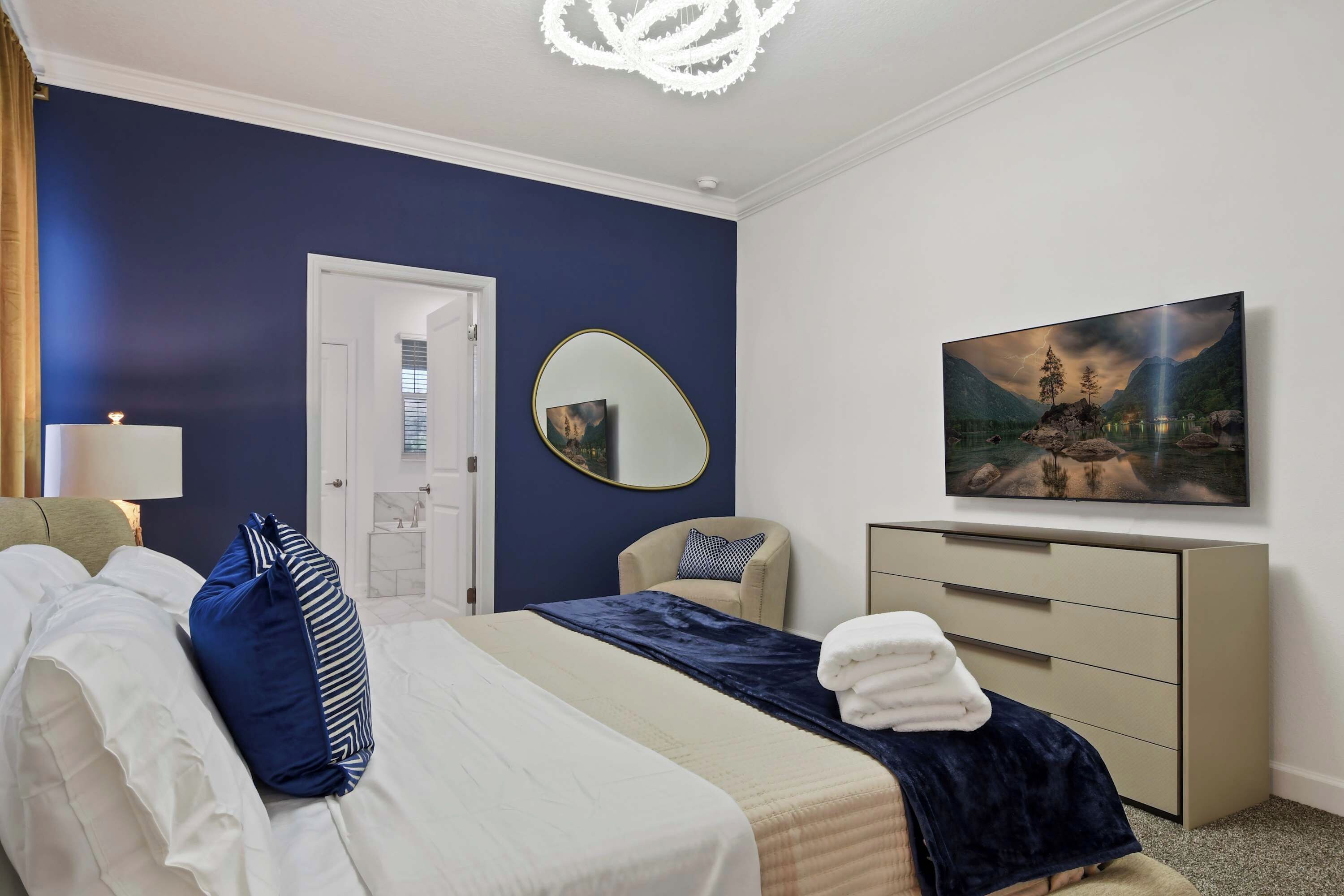 A hotel room with a bed, a bedside lamp, a TV, a mirror, and a dresser.