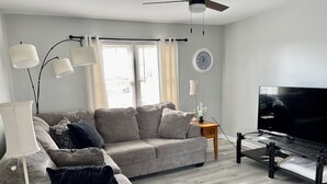 Sala de estar com sofá cinza, televisão, ventilador de teto e janela com cortinas.