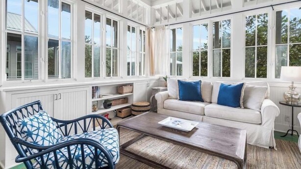 Una habitación iluminada por el sol con un sofá blanco, un sillón estampado azul y una mesa de centro.