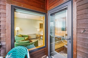 A wooden exterior wall with a sliding glass door leading to a room with a green sofa, a lamp, and a wooden table.