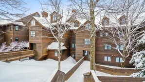 Een meerlaags houten gebouw met een besneeerd landschap, houten leuningen en een heldere lucht.