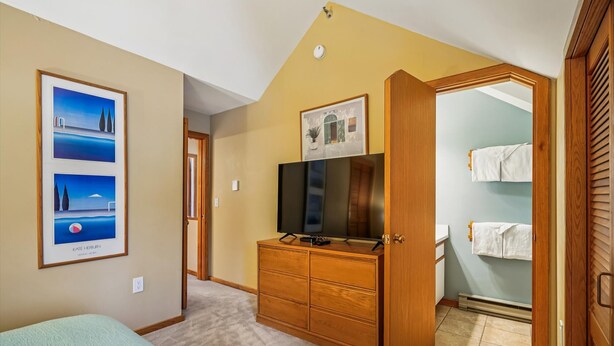 Een slaapkamer met een bed, een dressoir, een televisie en een inloopkast.