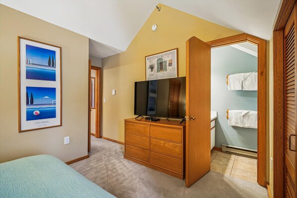 A bedroom with a bed, a dresser, a TV, and a closet. - 2 bedroom condo with mountain views, weekend shuttle, pool, and hot tub. (Killington)