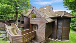 Una cabaña de madera con una escalera que lleva a una terraza, rodeada de árboles.