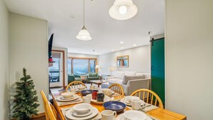 Comedor con una mesa de madera dispuesta para cuatro, un pequeño árbol de Navidad y vistas al exterior a través de amplios ventanales.