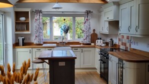 Een moderne keuken met een centraal eiland, houten balken, witte kasten en een groot raam met gordijnen.
