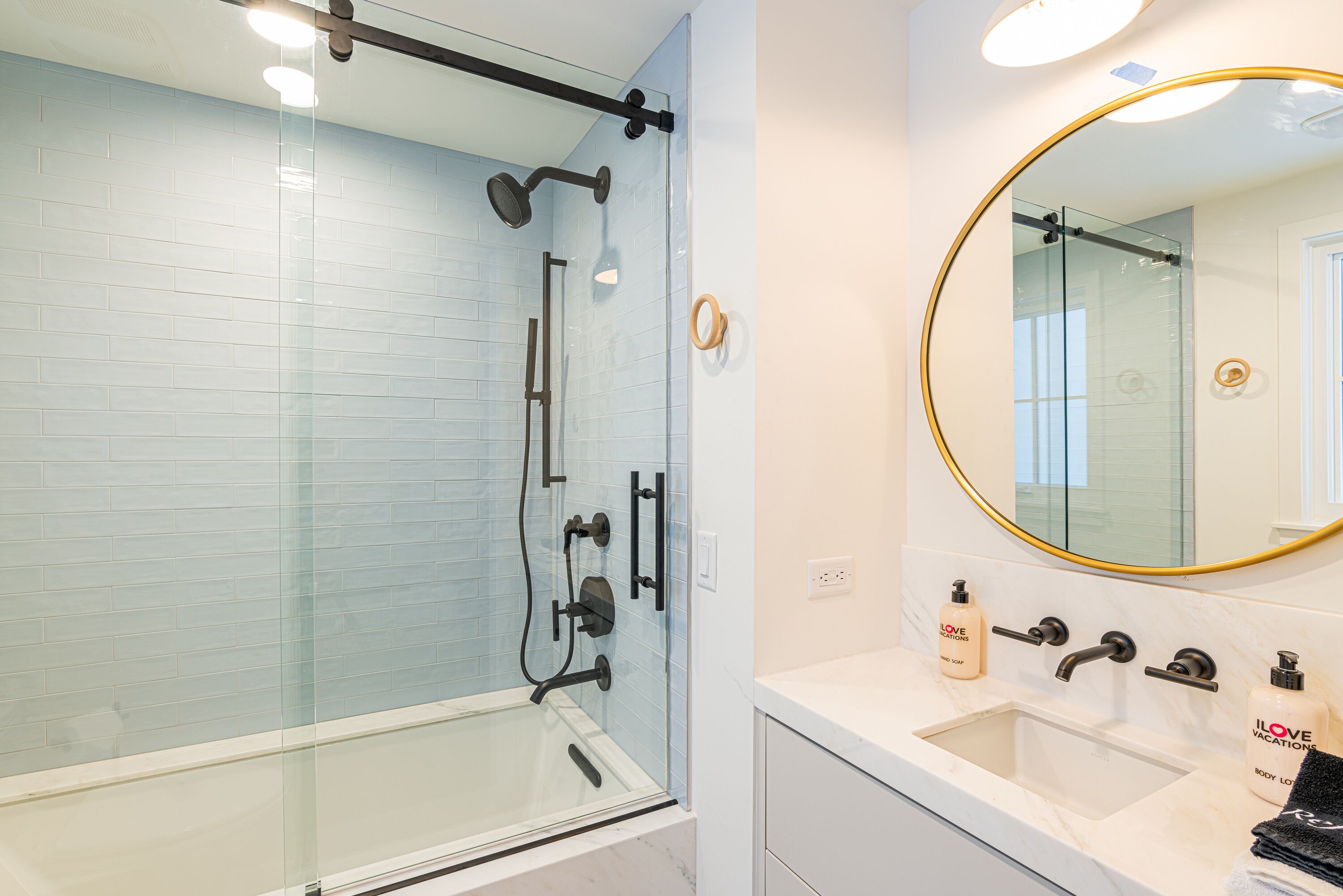 A modern bathroom with a glass-enclosed shower, a white sink, and a large mirror with a gold frame.
