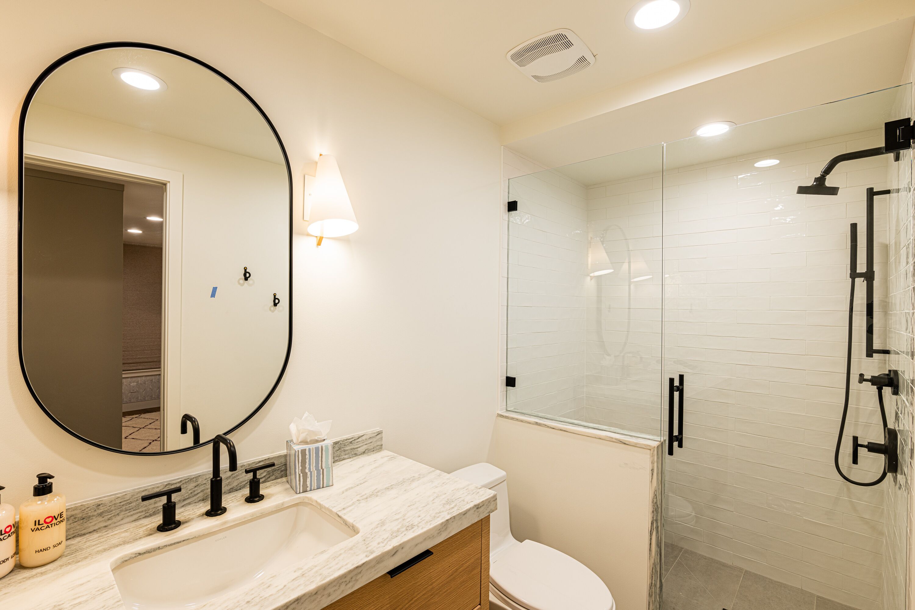 A modern bathroom with a large mirror, a sink with a marble countertop, a toilet, and a glass-enclosed shower area.
