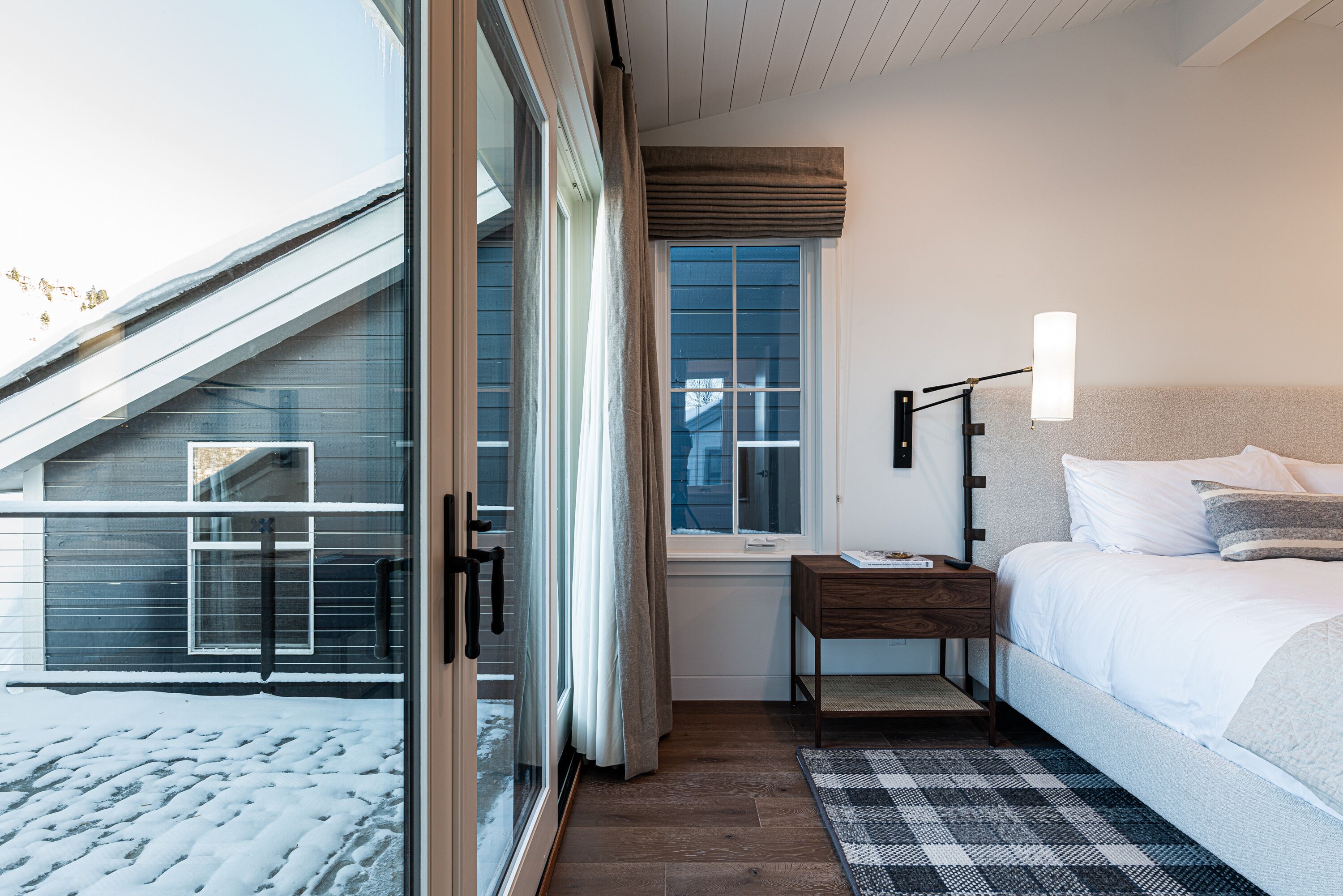 Une chambre à coucher avec un lit, une table de chevet, une lampe, une fenêtre et une vue sur l’extérieur.
