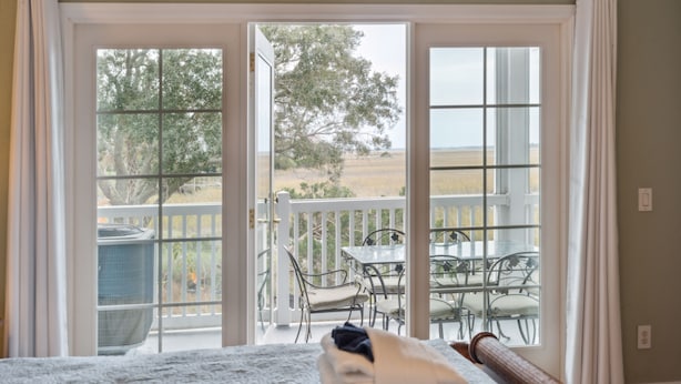A bedroom with a large window and sliding doors leading to a balcony with outdoor furniture.