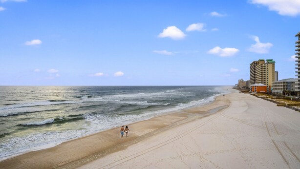Une plage avec un rivage sablonneux, des vagues et des bâtiments en arrière-plan.