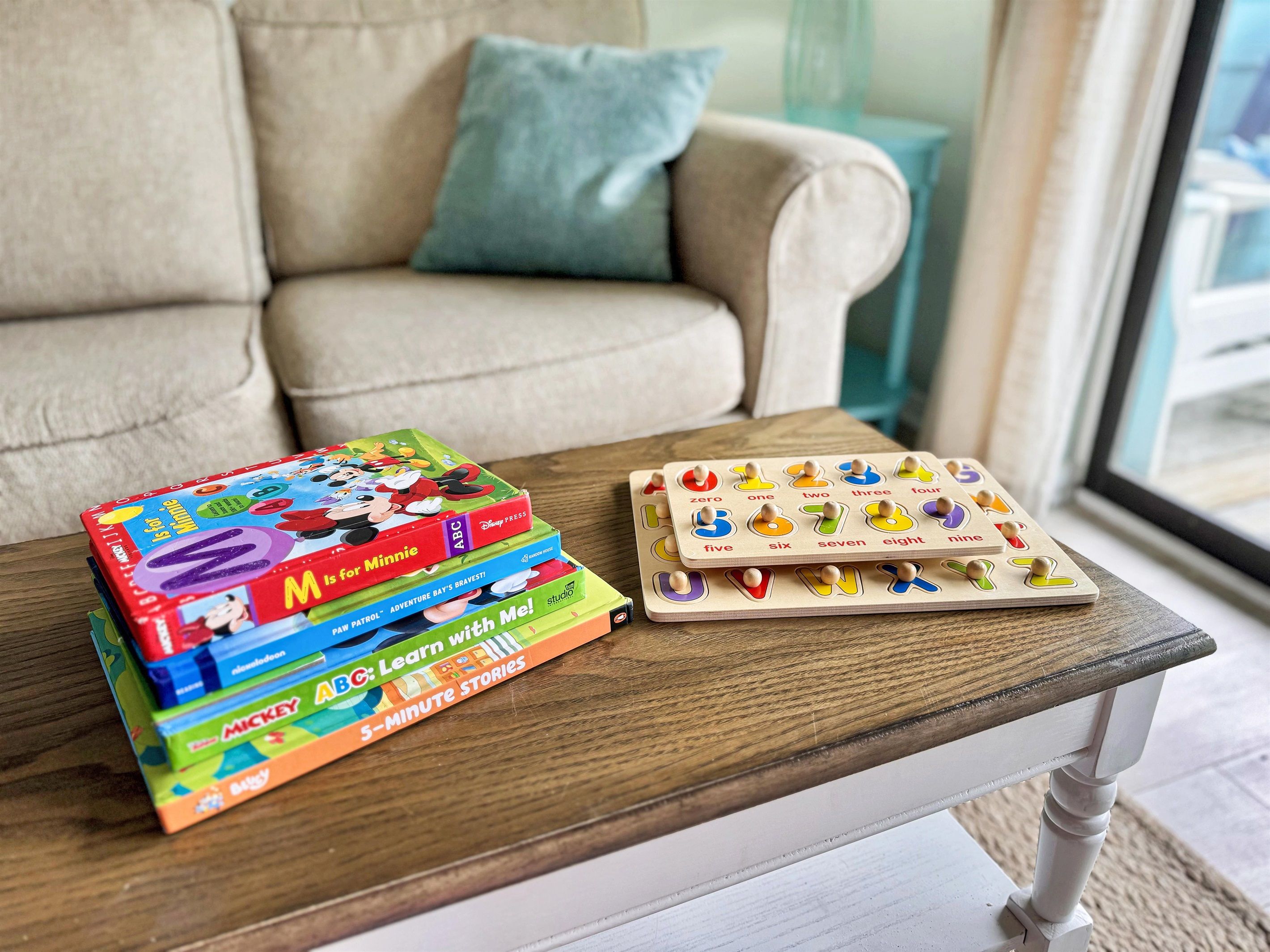 A stack of children's books and a wooden number board on a wooden table.