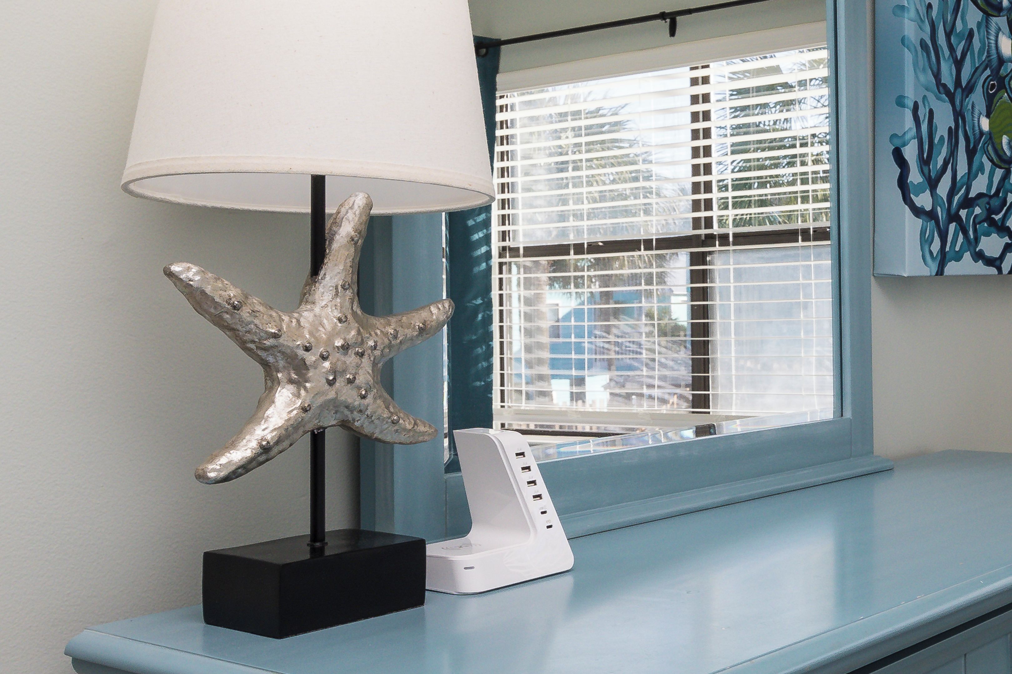 A room with a starfish decoration on a black stand, a white charging station, and a window with blinds.