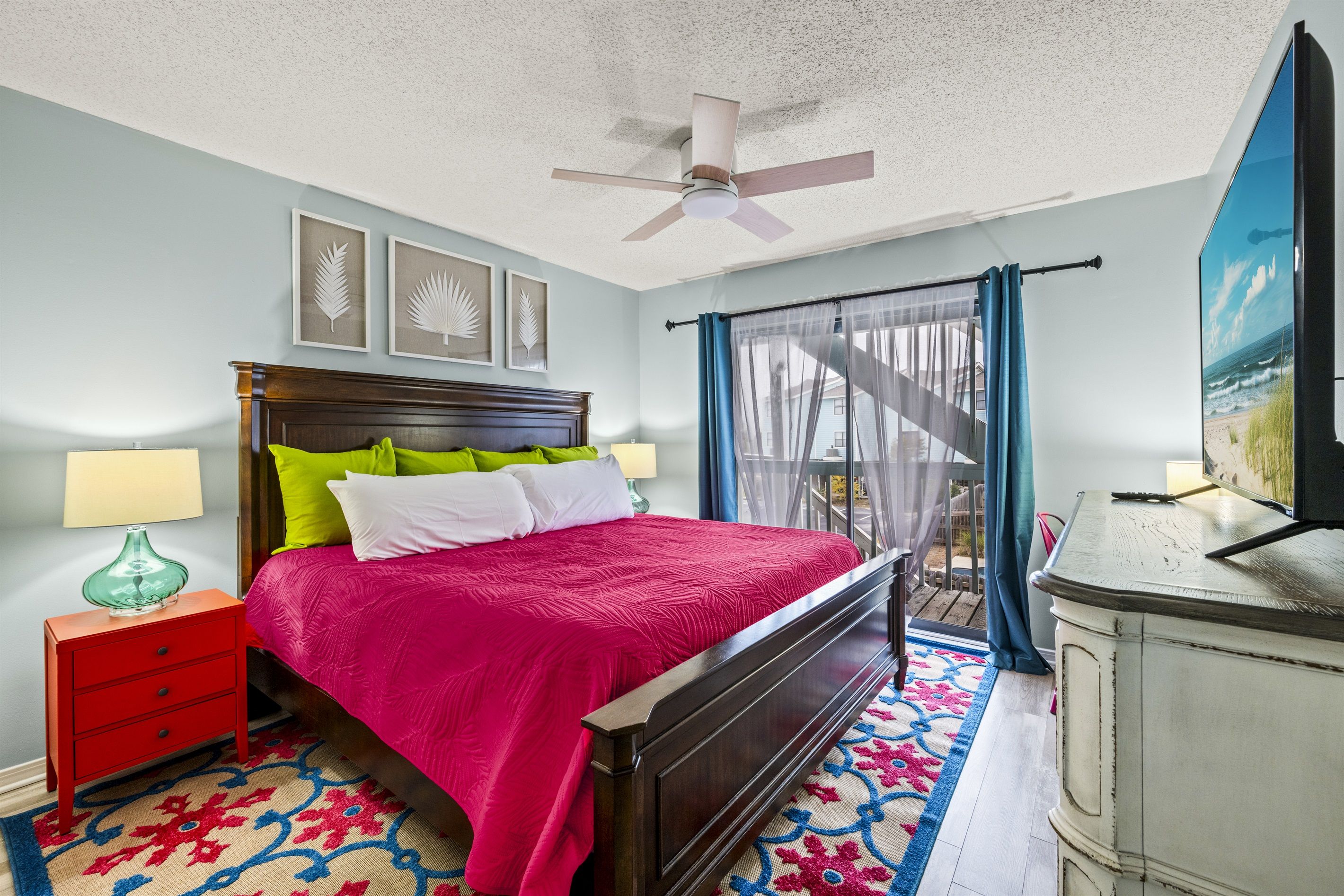 Une chambre à coucher comprenant un lit, une table de chevet, une commode, un ventilateur de plafond et une vue sur l’extérieur par une fenêtre.