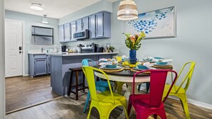 Une cuisine moderne avec des meubles gris, un îlot central et un coin repas agrémenté de chaises colorées.