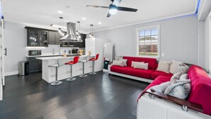 A modern kitchen with a central island, bar stools, and a red sofa in a spacious living area.