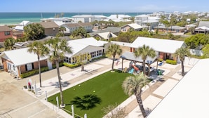 A residential area with houses, a grassy lawn, and a beach in the background.