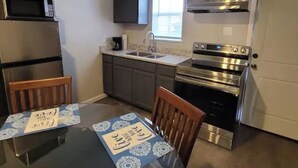 A compact kitchen with a microwave, stove, and sink. There is a table with a placemat and two chairs. - Luxury Apartment Suite 5 (El Paso)