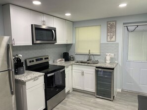 A modern kitchen with white cabinets, a stainless steel refrigerator, a microwave, a stove, and a dishwasher.
