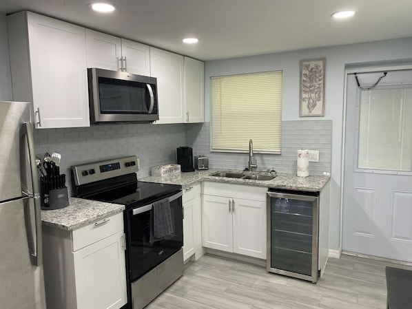A modern kitchen with white cabinets, a stainless steel refrigerator, a microwave, a stove, and a dishwasher.