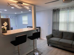 A modern kitchen with a bar area, a sofa, and a dining table.