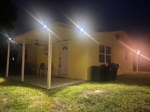 A house with a covered porch and a door, illuminated by exterior lights.