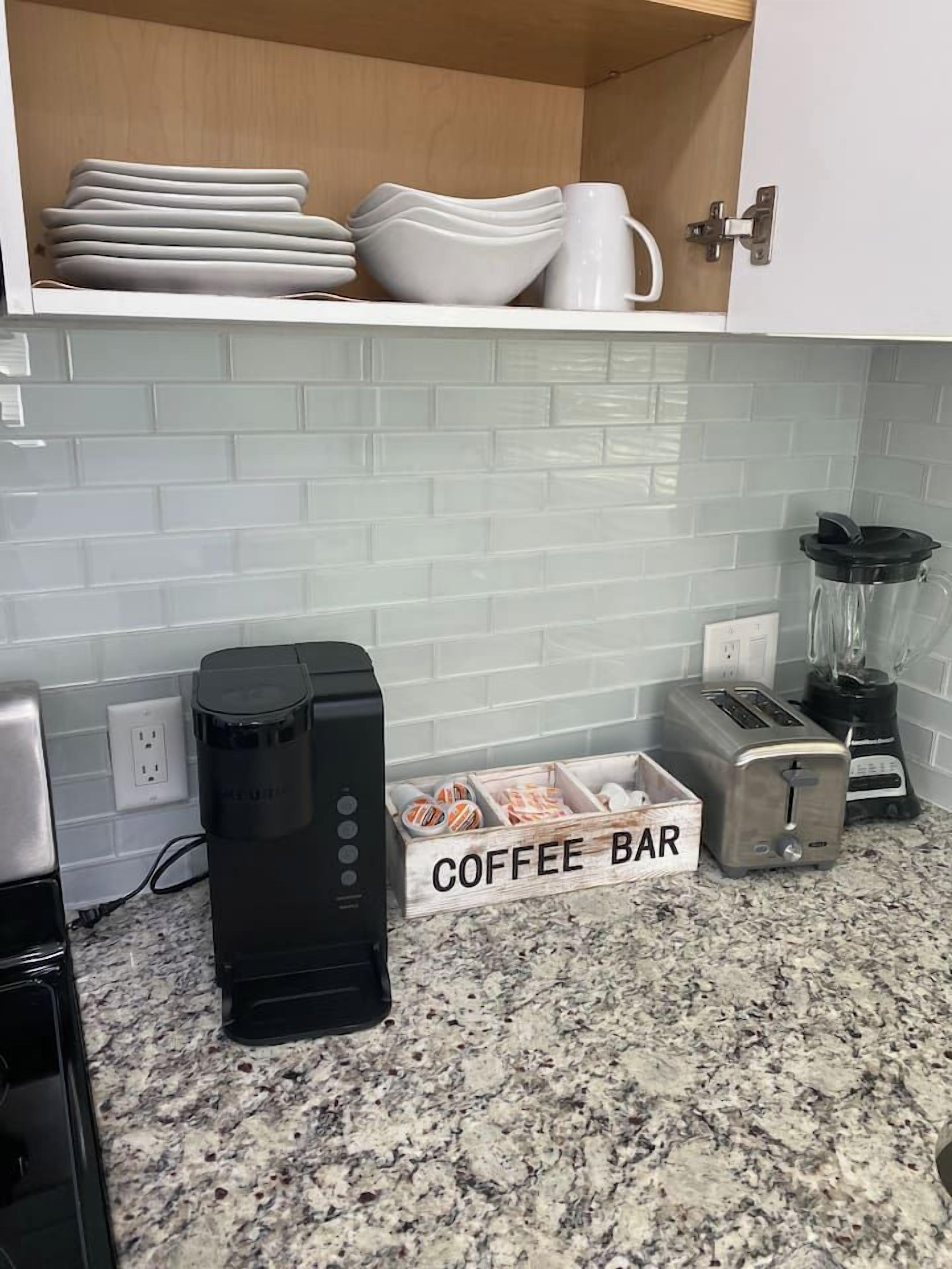 Et køkken med kaffemaskine, brødrister, blender og en kaffebars beholder.