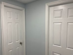Deux portes blanches au design simple, l’une dotée d’un bouton de porte rond et l’autre d’une poignée ronde, sur un mur uni.