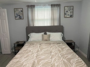 A bedroom with a bed, two bedside tables, a nightstand, a door, and two wall-mounted paintings.