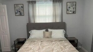 A bedroom with a bed, two bedside tables, a window with curtains, and two wall-mounted paintings. - Modern 2/1 Sleeps 6 Quiet Dead End St 1/2 Acre Wow (Parrish)