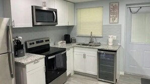 A modern kitchen with white cabinets, a stainless steel refrigerator, a microwave, an oven, a sink, and a dishwasher. - Modern 2/1 Sleeps 6 Quiet Dead End St 1/2 Acre Wow (Parrish)
