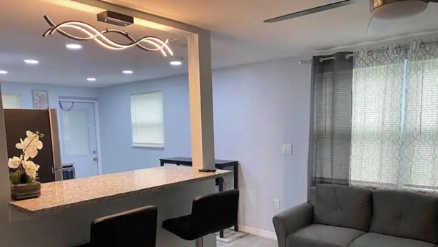 A modern living room with a grey sofa, a bar area with two stools, and a large window with blinds. - Modern 2/1 Sleeps 6 Quiet Dead End St 1/2 Acre Wow (Parrish)