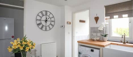 A modern kitchen with a built-in washing machine, a large wall clock, and a window with a checkered valance.