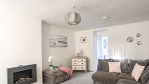 Ein Wohnzimmer mit Kamin, einem grauen Sofa, einer weißen Kommode und einer Pendelleuchte.
